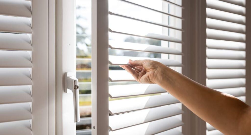 Hand adjusting white plantation shutters