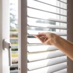 Hand adjusting white plantation shutters